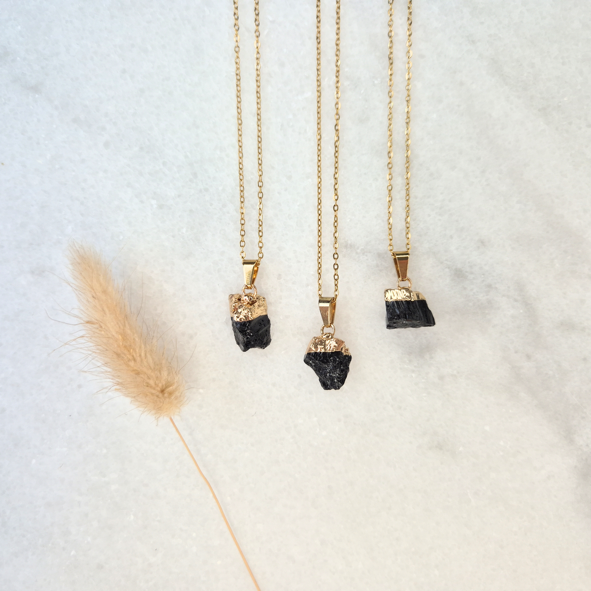 Three gold-plated necklaces with natural raw black tourmaline pendants, each with a unique shape and size.