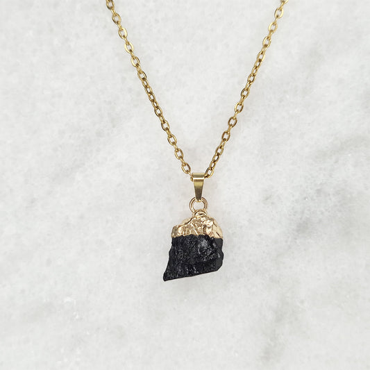 Close-up of a raw black tourmaline pendant with a gold-tone setting, hanging from a gold-plated necklace.